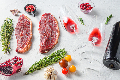 Two glasses of red wine near bottle and beef steaks over white concrete background, side view