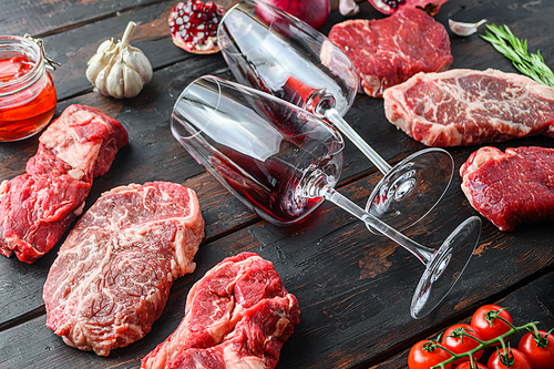 Meat beef steaks frame concept, with different steak cuts and two wine glasses in frame on dark old wooden table  side view