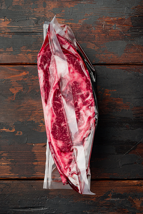 Pack with fresh beef steak cut for sous vide in vacuum plastic market bag set, on old dark  wooden table background, top view flat lay