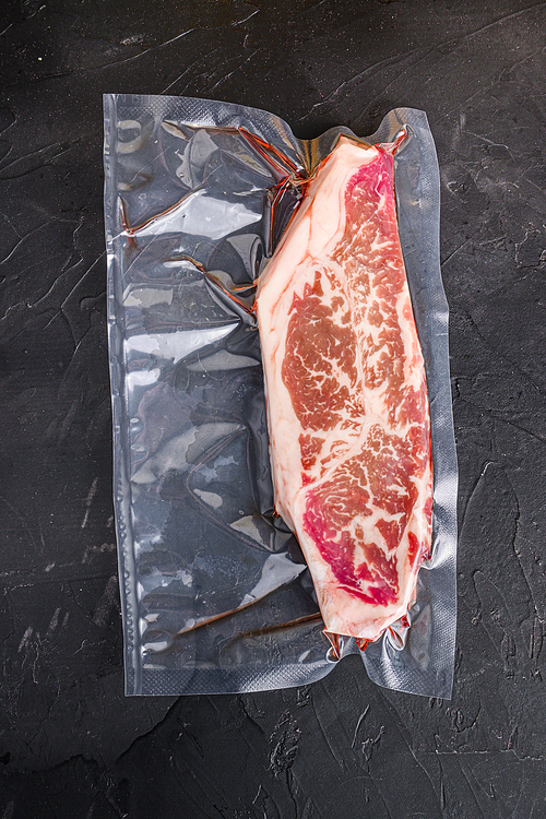 Vacuum packed organic beef  top blade steak for sous vide cooking  on black textured background, top view
