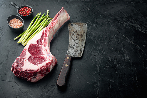 Uncooked raw beef red meat marbled with bone in set, and old butcher cleaver knife, with grill ingredients, on black stone background, with copy space for text