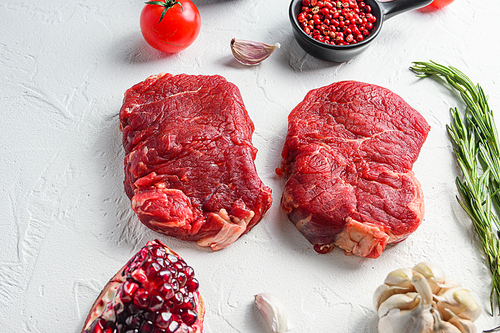 Raw rumpsteak, farm beef meat with seasonings, rosemary, garlic, garnet. White textured background. Side view