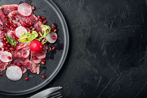 Beef Carpaccio cold appetizer set, with Radish and garnet, on plate, on black stone background, top view flat lay, with copy space for text