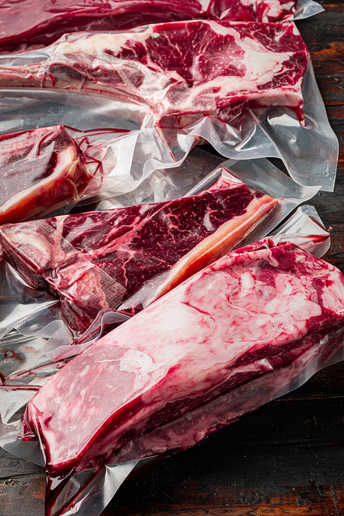 Raw marbled beef steak in vacuum packaging set, tomahawk, t bone, club steak, rib eye and tenderloin cuts, on old dark  wooden table background