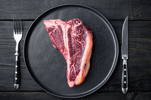 Prime cut tender raw t bone steak for a BBQ set, on plate, on black wooden table background, top view flat lay