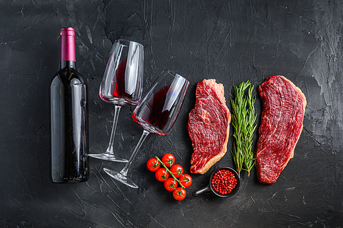 Raw picanha steaks with seasonings and herbs near bottle and glass of red wine, over black textured table top view