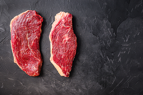 Organic raw picanha beef steaks, on black textured background, top view with space for text