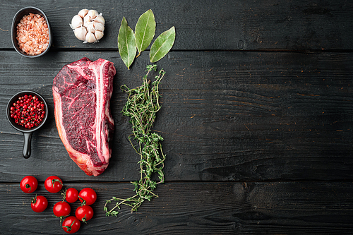 Raw club steak with ingredients set on black wooden table background, top view flat lay, with copy space for text