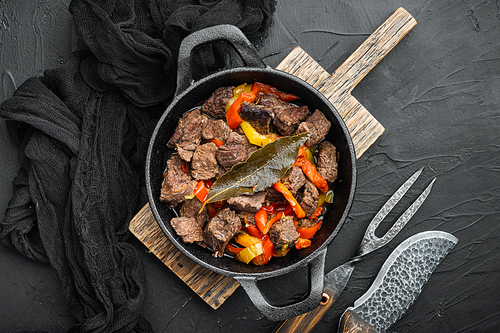 Bangin beef stew served, in cast iron frying pan, on black stone background, top view flat lay, with copy space for text