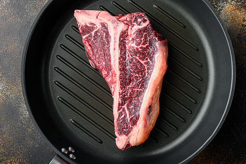 Raw fresh beef t-bone steak drya aged cut set, in frying cast iron pan, on old dark rustic background, top view flat lay