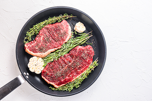 Two raw picanha organic  beef steaks ready for grill on pan with herbs and garlic. Over white textured background, top view with space for text