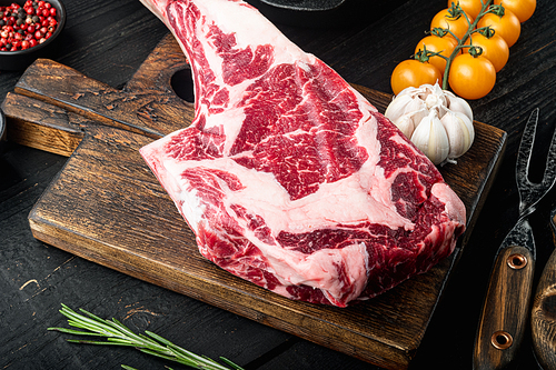 Raw uncooked black angus beef tomahawk steak on bone set, with grill ingredients, on black wooden table background