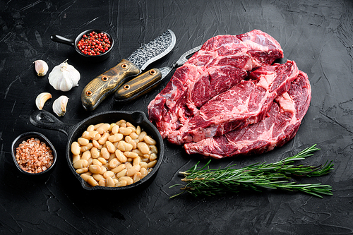 Raw rib eye beef marbled meat  steak with pepper and herbs set, on black stone background