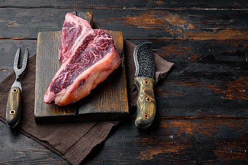 Raw fresh dry aged beef T-bone steak set, on wooden cutting board, on old dark  wooden table background, with copy space for text