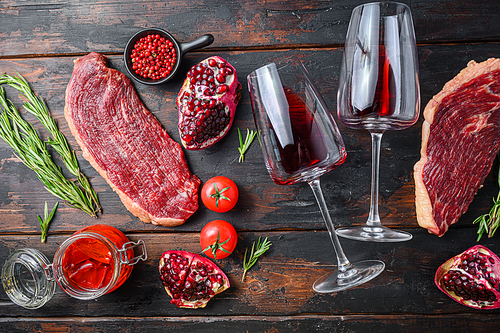 Raw picanha beef steak with rosemary, spicy chili oil, pomegranate and glass of red wine, on old dark wooden table top view