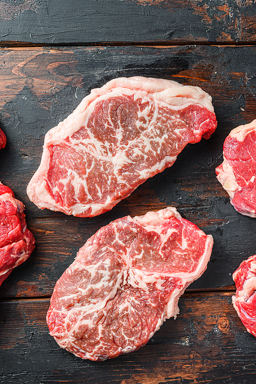 Variety of organic raw beef steakes, top blade cut on old rustic dark wooden background, top view