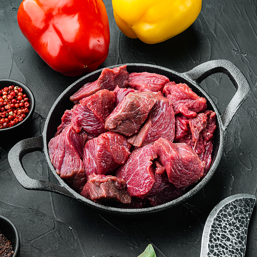 Beef casserole or goulash ingredients set with sweet bell pepper, in cast iron frying pan, on black stone background