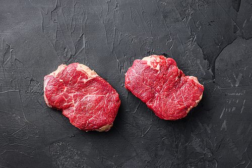 Set of raw rump steaks over black textured  background, top view