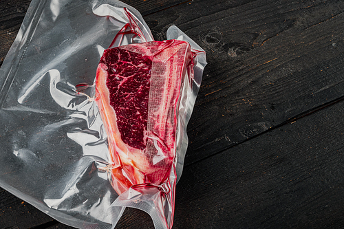 Dry aged beef marbled meat, raw fresh club beefsteak in plastic package set, on black wooden table background, with copy space for text