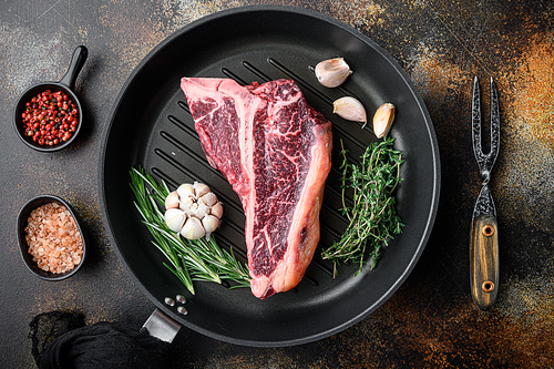 Cooking meat background. Raw aged beef t-bone steak, with spices and herbs for grill set, on frying cast iron pan, on old dark rustic background, top view flat lay