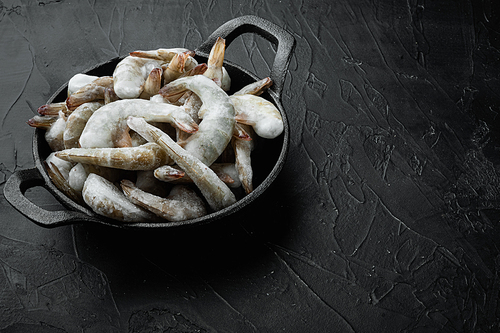 Frozen raw uncooked tiger prawns, shrimps set, in cast iron frying pan, on black stone background, with copy space for text