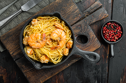 Tasty appetizing pasta spaghetti with pesto sauce and shrimps set, in cast iron frying pan, on old dark  wooden table, top view flat lay