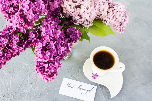 Cup of morning coffee and purple lilac flowers on grey concrete background