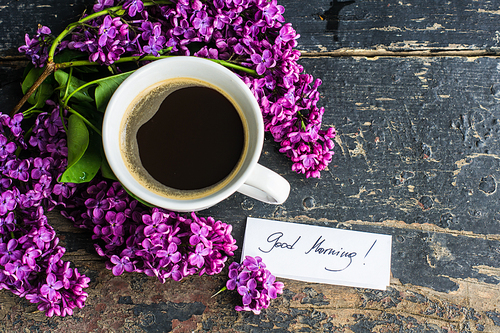Cup of morning coffee and purple lilac flowers on dark wooden background