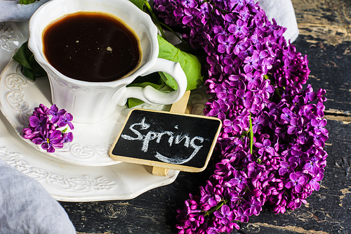 Cup of morning coffee and purple lilac flowers on dark wooden background