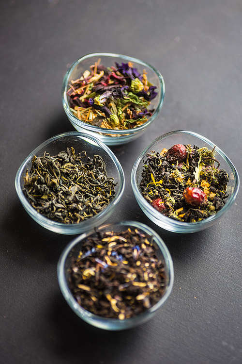 Different types of tea, green tea, peony and ginger tea, rose bud and wild flowers tea on dark wooden background with copyspace