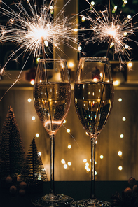 Two glasses of sparkling wine champagne with sparklers. Dark background with yellow light bokeh. Christmas tree toys on the table. New Year's bengal fire. Christmas winter holidays