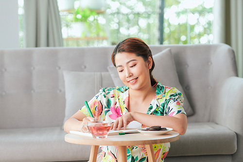 Relaxed woman sitting on floor in livingroom writing in diary