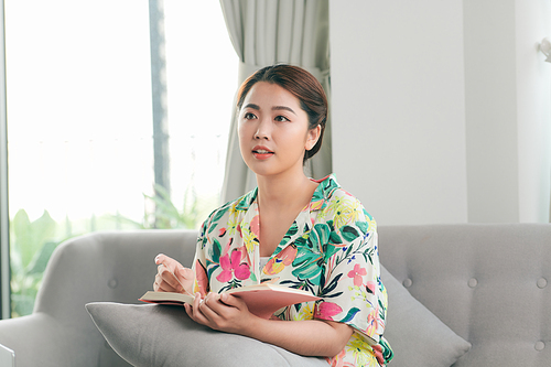 A young woman is reading a book while sitting on a sofa.