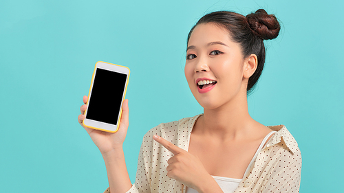 Portrait of an excited young woman showing blank screen mobile phone isolated over turquoise background