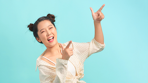 Young asian woman standing over background smiling and looking at the camera pointing with two hands and fingers to the side.