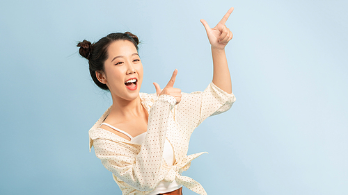 Portrait of a smiling young asian woman pointing fingers away at copy space isolated over blue background