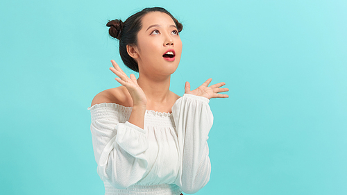 Close-up portrait of amused, surprised asian girl receive incredible good news, touch cheeks and smiling amused, glad to win, triumphing, blue background