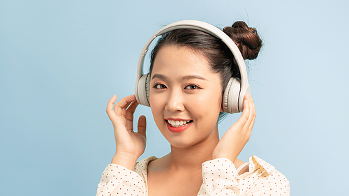 Happy cute young woman in headphones listening to music over blue background