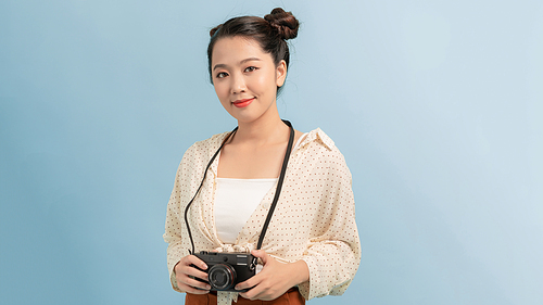 Portrait of a smiling young woman standing with photo camera and looking away at copy space isolated over blue background