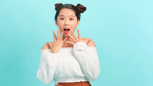 Close-up portrait of amused, surprised asian girl receive incredible good news, touch cheeks and smiling amused, glad to win, triumphing, blue background