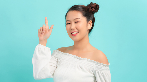 Close-up of joyful woman winking when pointing an index finger over blue background.