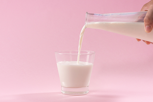 Pouring milk in to glass from bottle on a pink