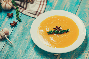 Pumpkin and carrot soup with cream and parsley on blue  wooden background.