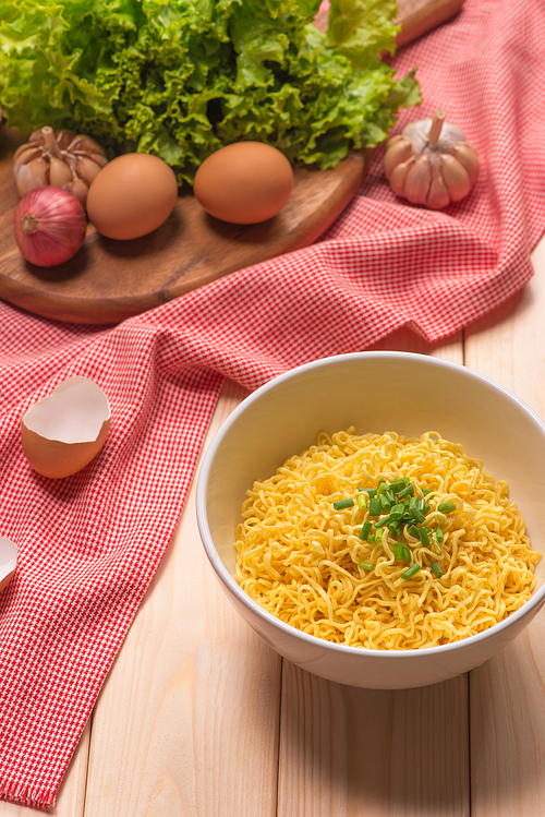 Instant noodles in bowl with vegetables on wood background