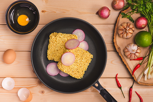 Instant noodles for cooking and eat in the dish with eggs and vegetables on wooden background.