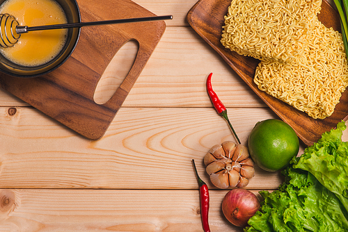 Instant noodles for cooking and eat in the dish with whipped egg and vegetables on wooden background.