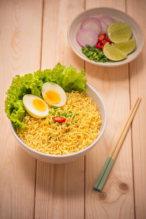 Instant noodles in bowl with vegetables and  boiled egg on wood background