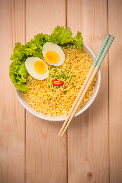 Instant noodles in bowl with vegetables and  boiled egg on wood background