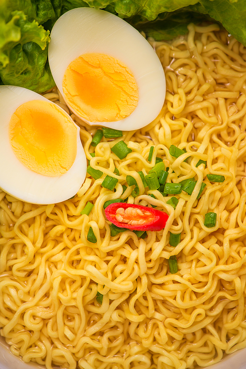 Instant noodles in bowl with vegetables and  boiled egg on wood background