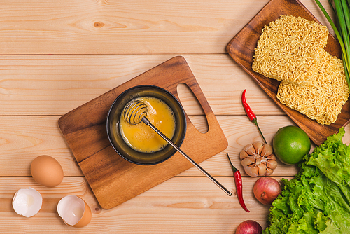 Instant noodles for cooking and eat in the dish with whipped egg and vegetables on wooden background.